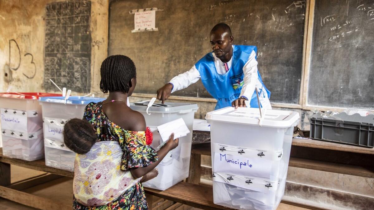 Un agent électoral aide un électeur à déposer son bulletin.
