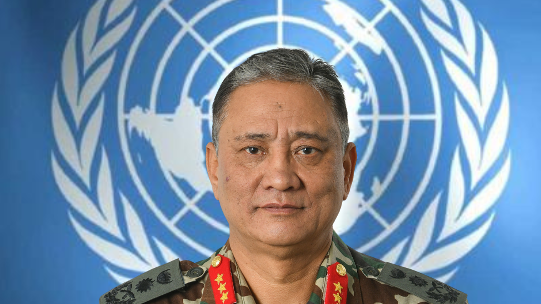 A headshot of a man in military uniform against a background showing the UN logo