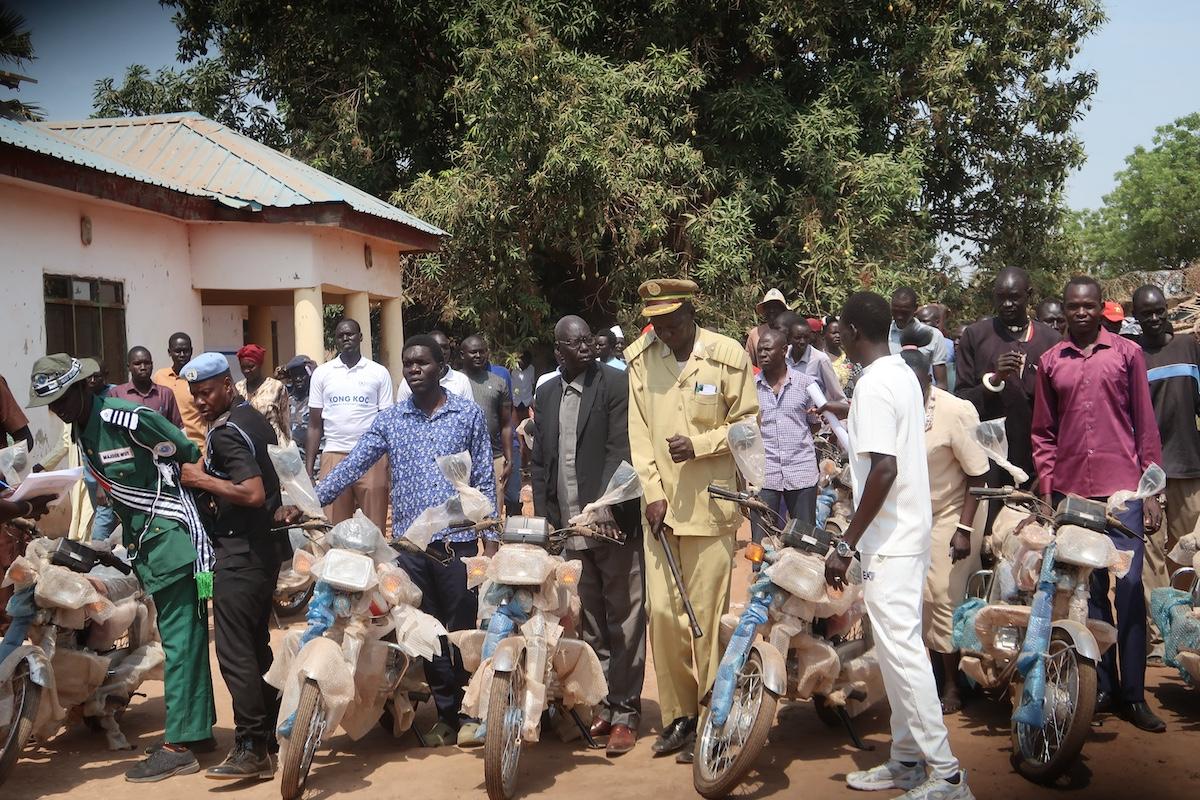 A group of people standing in a line holding motorbikes